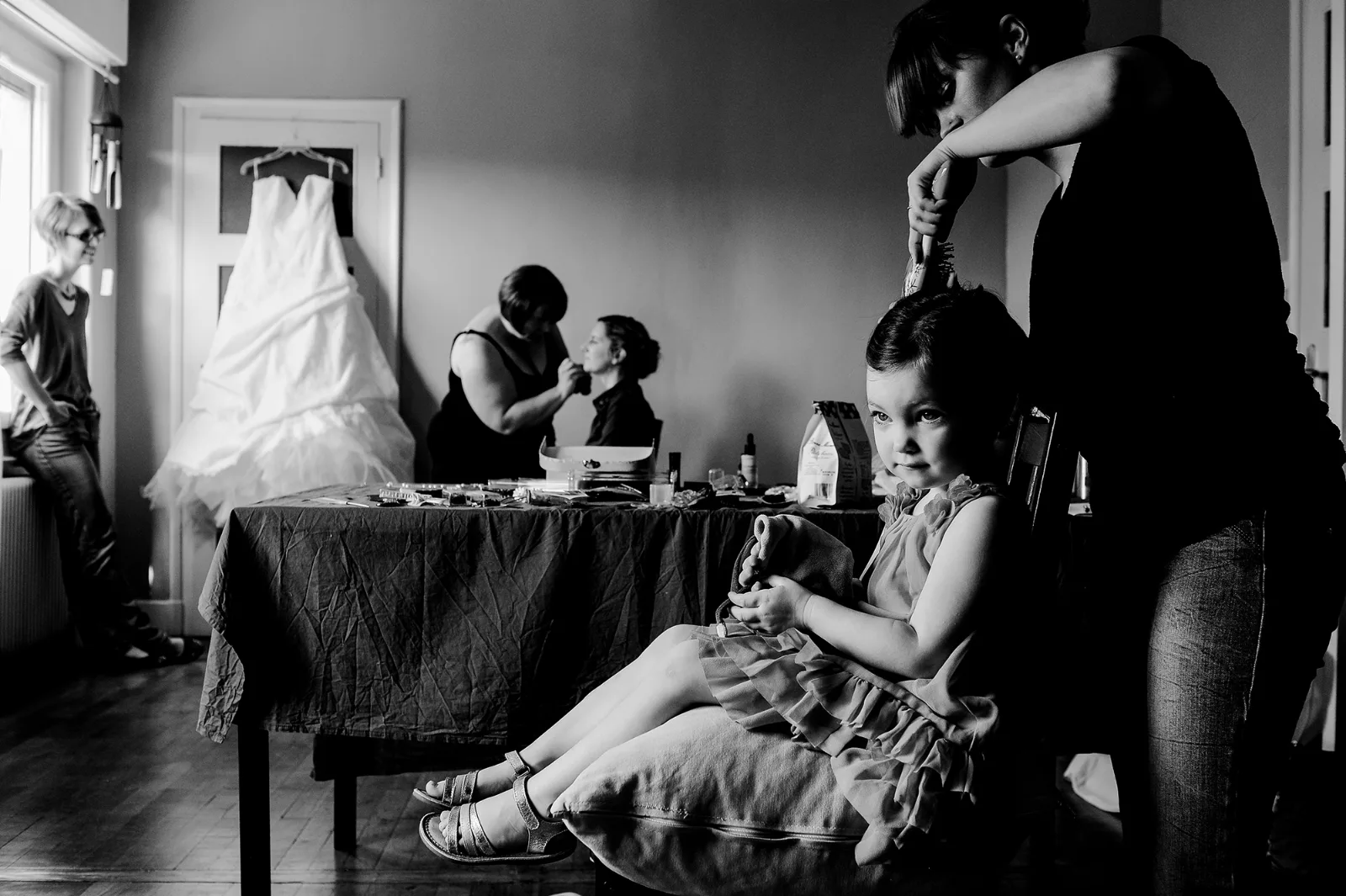 Préparatifs de la mariée en noir et blanc : robe suspendue, maquillage et petite fille