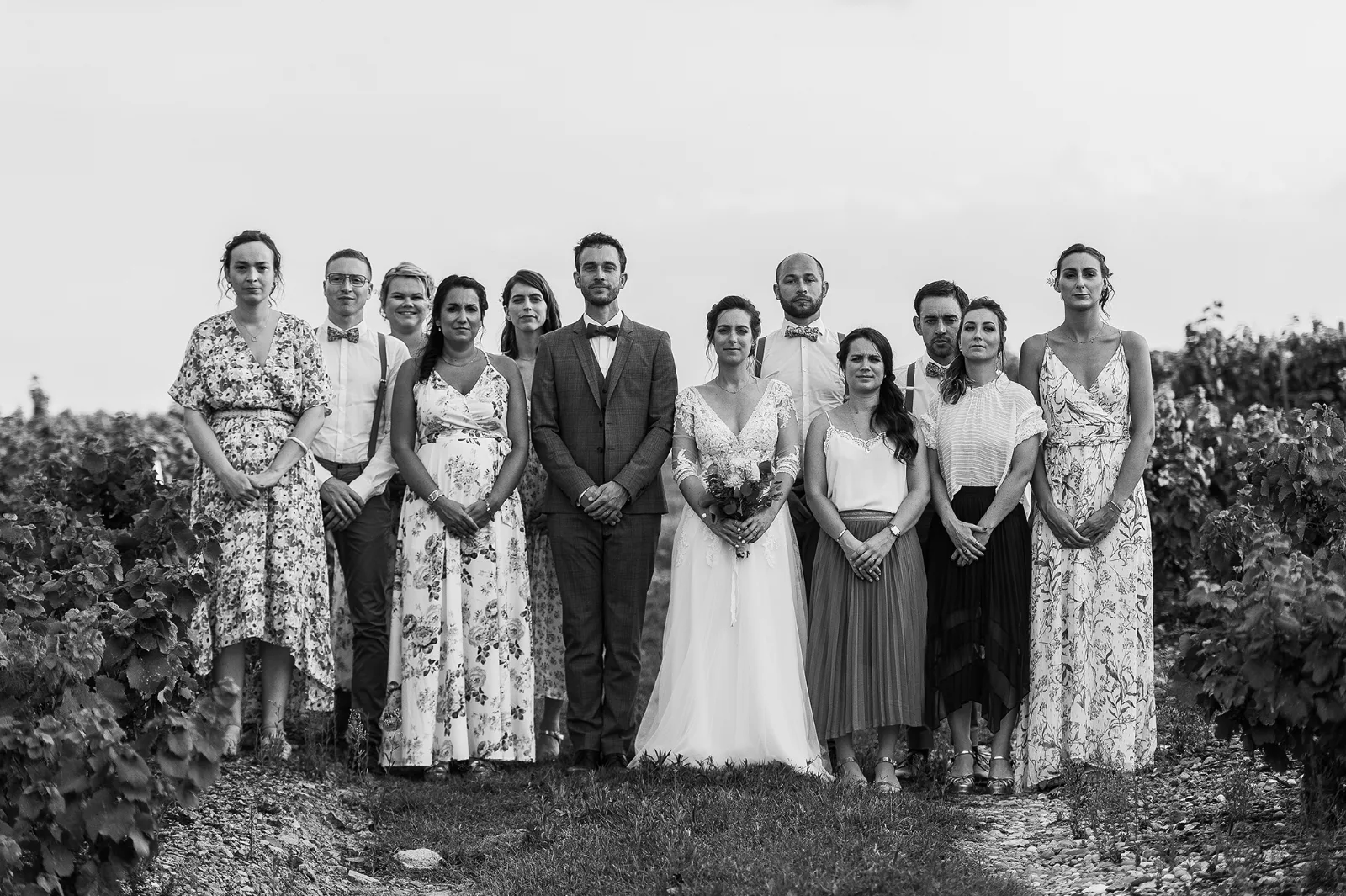 Photo de groupe des mariés et de leurs invités en noir et blanc devant un paysage