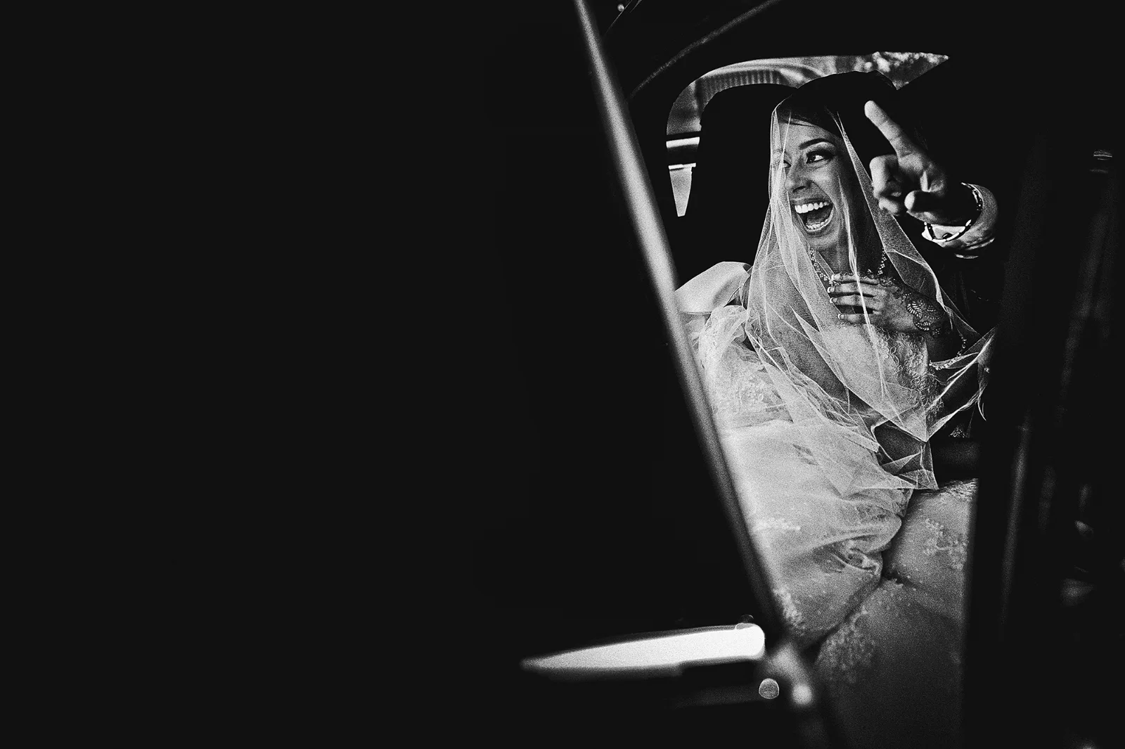 Mariée voilée à la portière d'une voiture sombre, noir et blanc