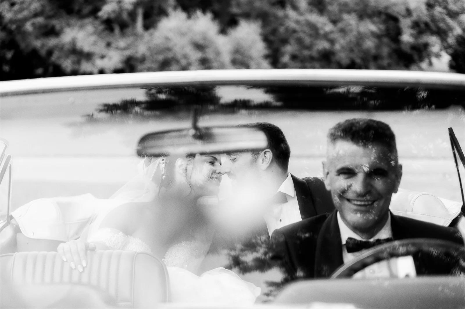 Marié souriant au volant d'une voiture de mariage, reflets, noir et blanc