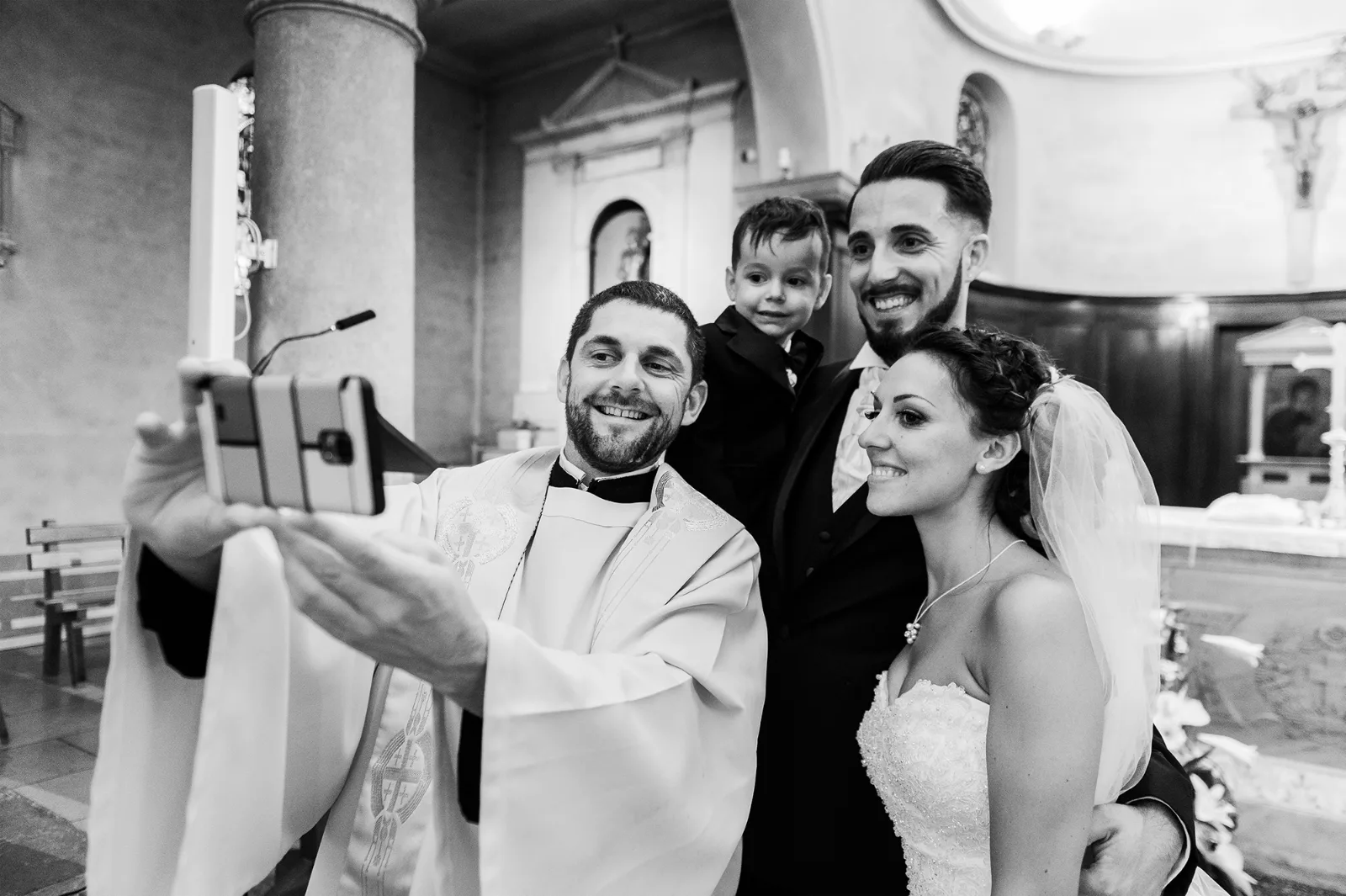 Prêtre, mariés et enfant prenant un selfie à la fin de la cérémonie, noir et blanc
