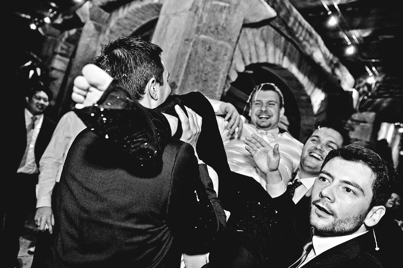 Invités en liesse portant le marié, ambiance de fête, noir et blanc