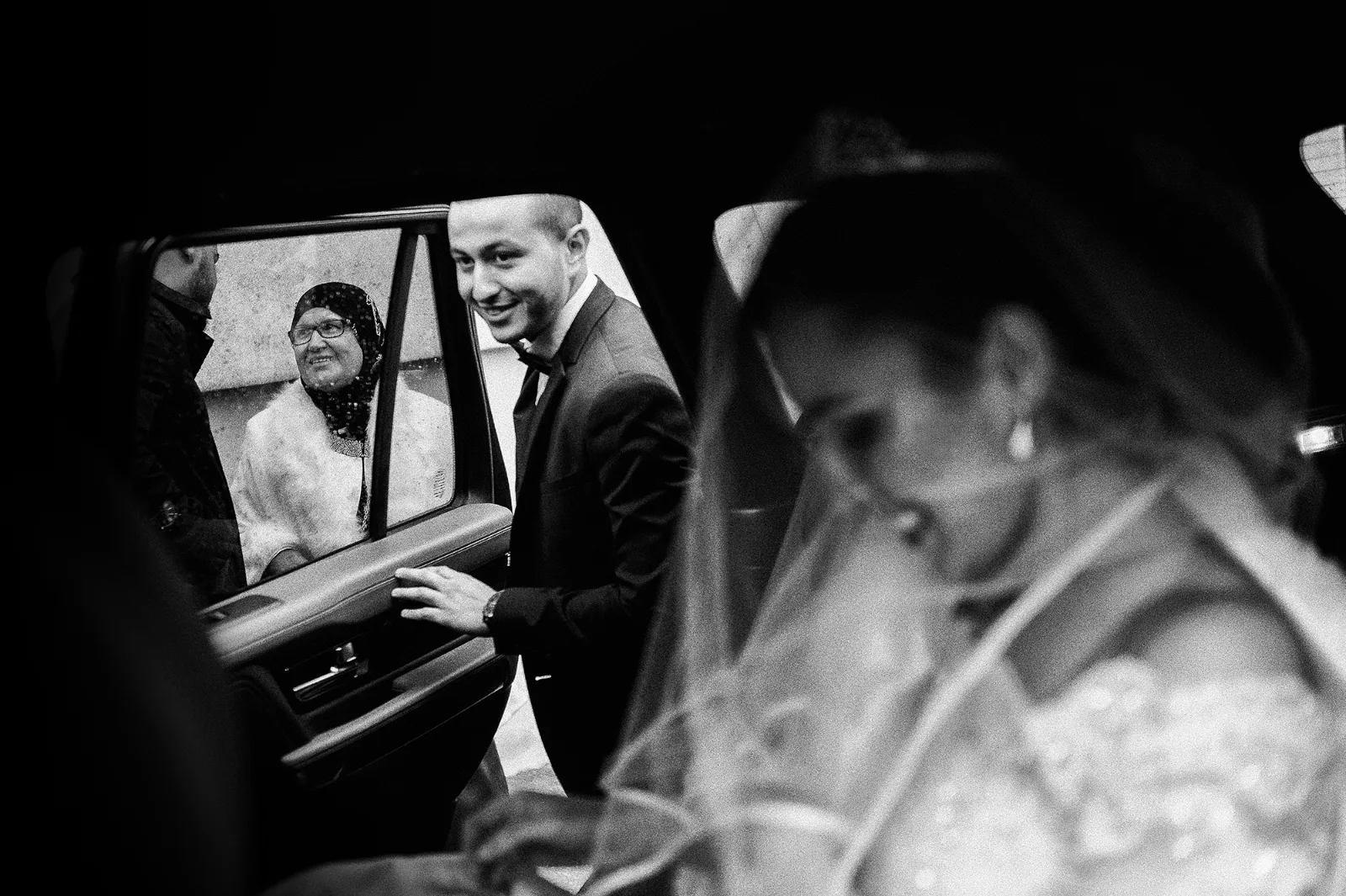Mariée émue à la portière d'une voiture, regard du marié, noir et blanc