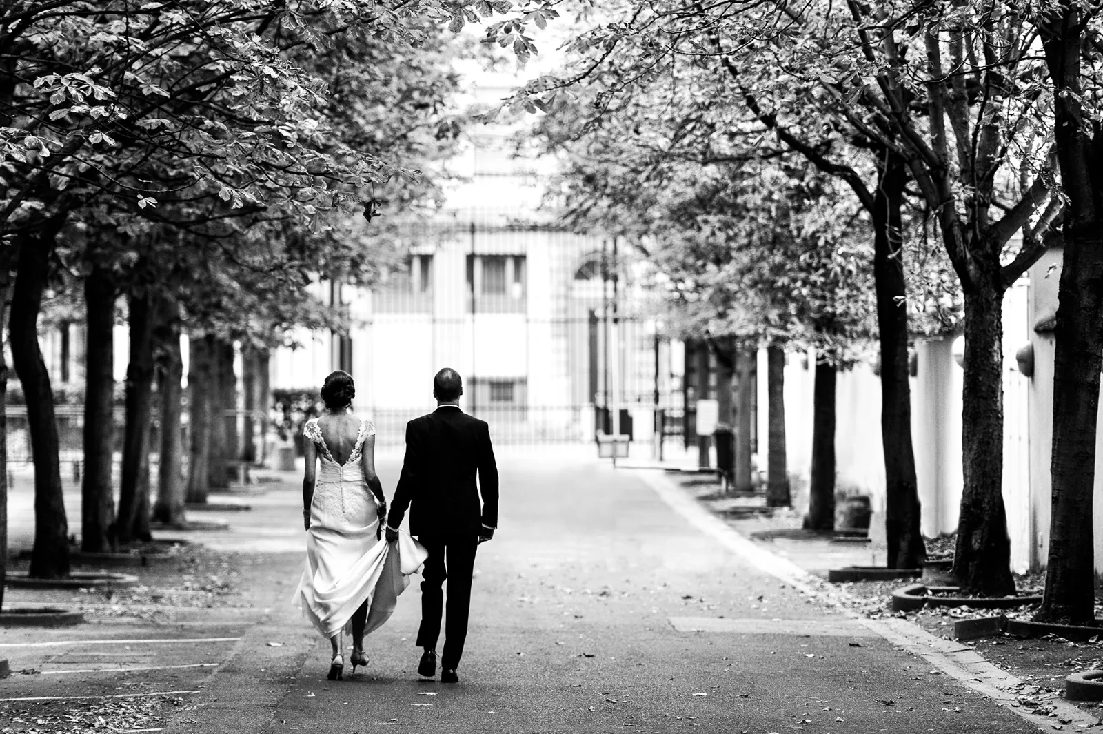 Mariés marchant dans une allée d'arbres, photographie de mariage en noir et blanc